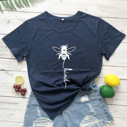 Navy blue t-shirt with white bee and 'be kind' print, paired with ripped denim shorts on wood background, surrounded by fruit for a casual summer look.