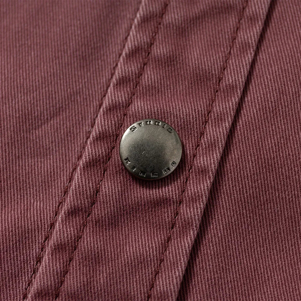 Close-up of metal snap button on brown textured fabric, detailed stitching visible