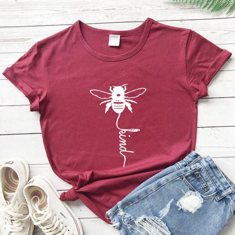 Red bee kind graphic t-shirt with denim shorts and white sneakers on wooden background