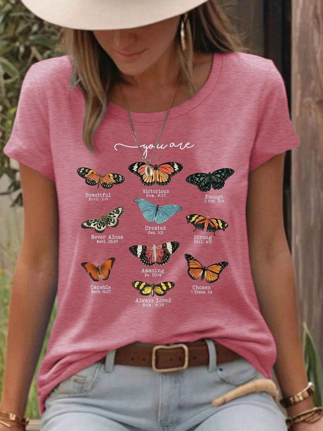 Woman wearing pink t-shirt with colorful butterfly graphics and inspirational words outdoors.