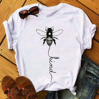 White t-shirt with bee graphic and 'kind' text, paired with sunglasses and sandals on wood