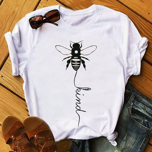 White t-shirt with bee graphic and 'kind' text, paired with sunglasses and sandals on wood