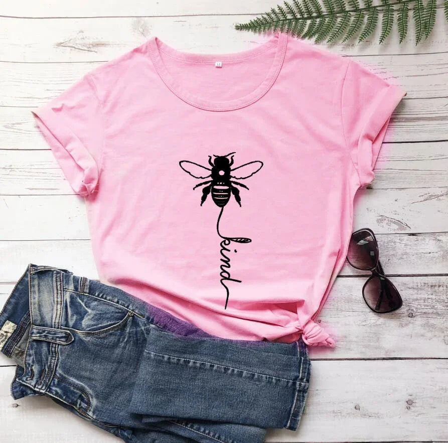 Pink t-shirt with bee and 'be kind' graphic, paired with denim shorts on wooden background