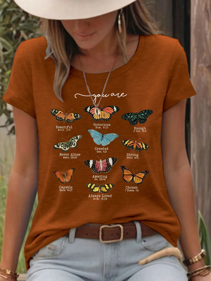 Woman wearing rust-colored t-shirt with butterfly and Bible verse graphic print outdoors
