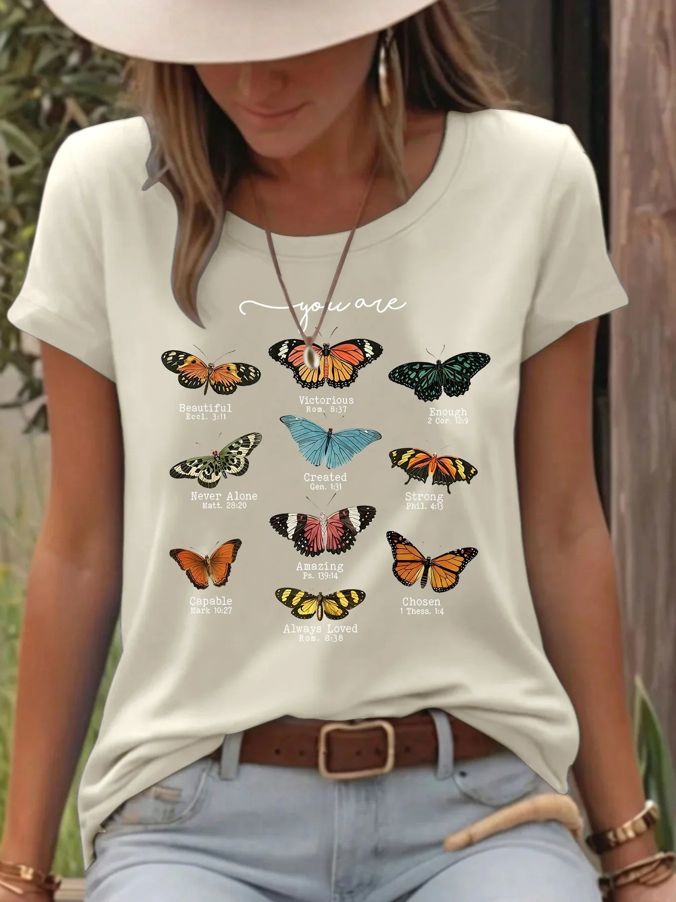 Woman outdoors wearing a beige t-shirt with colorful butterflies and positive inspirational words.