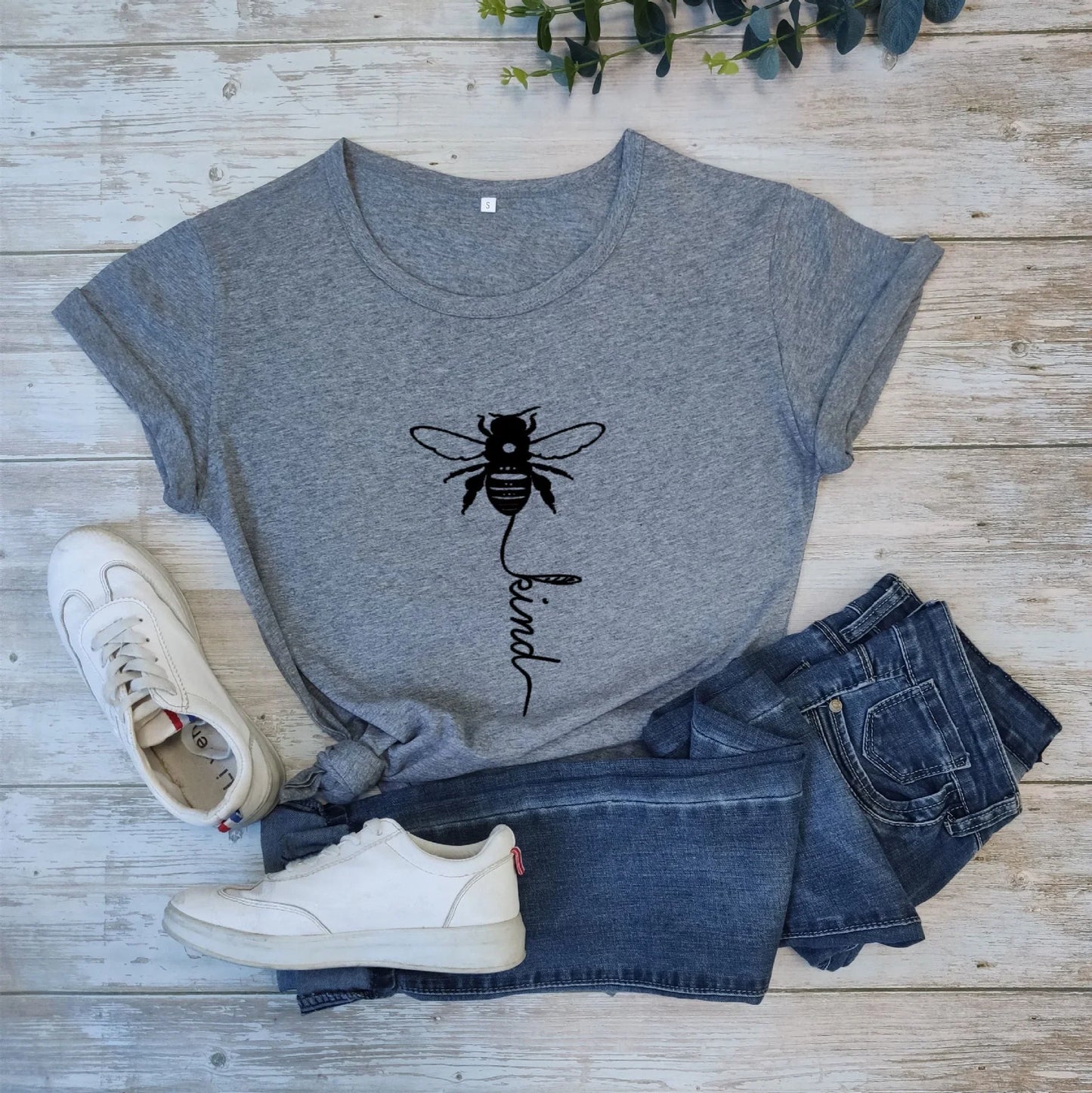 Gray t-shirt with bee kind graphic, paired with denim shorts and white sneakers on wood floor.