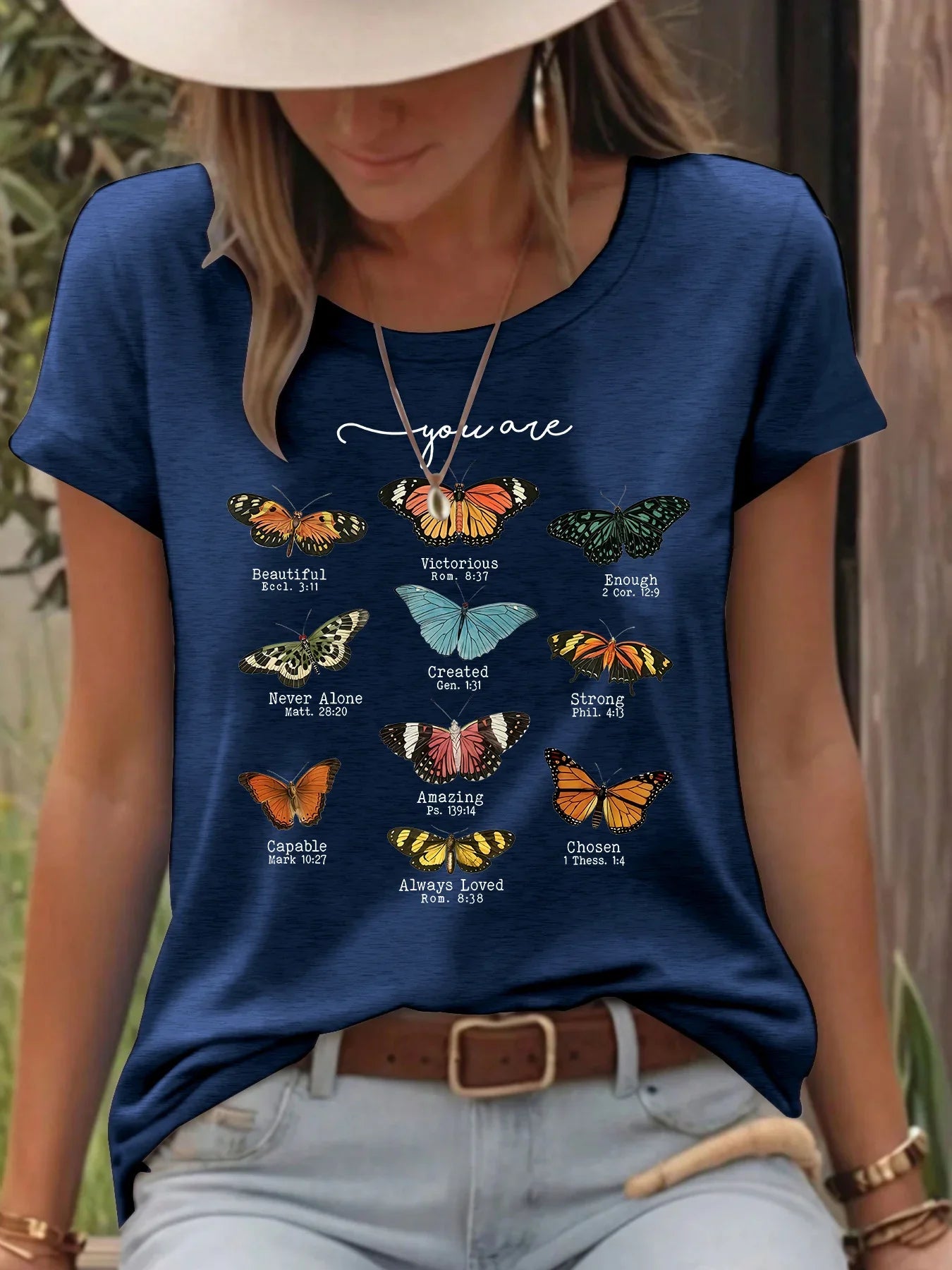 Woman wearing blue t-shirt with colorful butterflies and inspirational Bible verses outdoors.