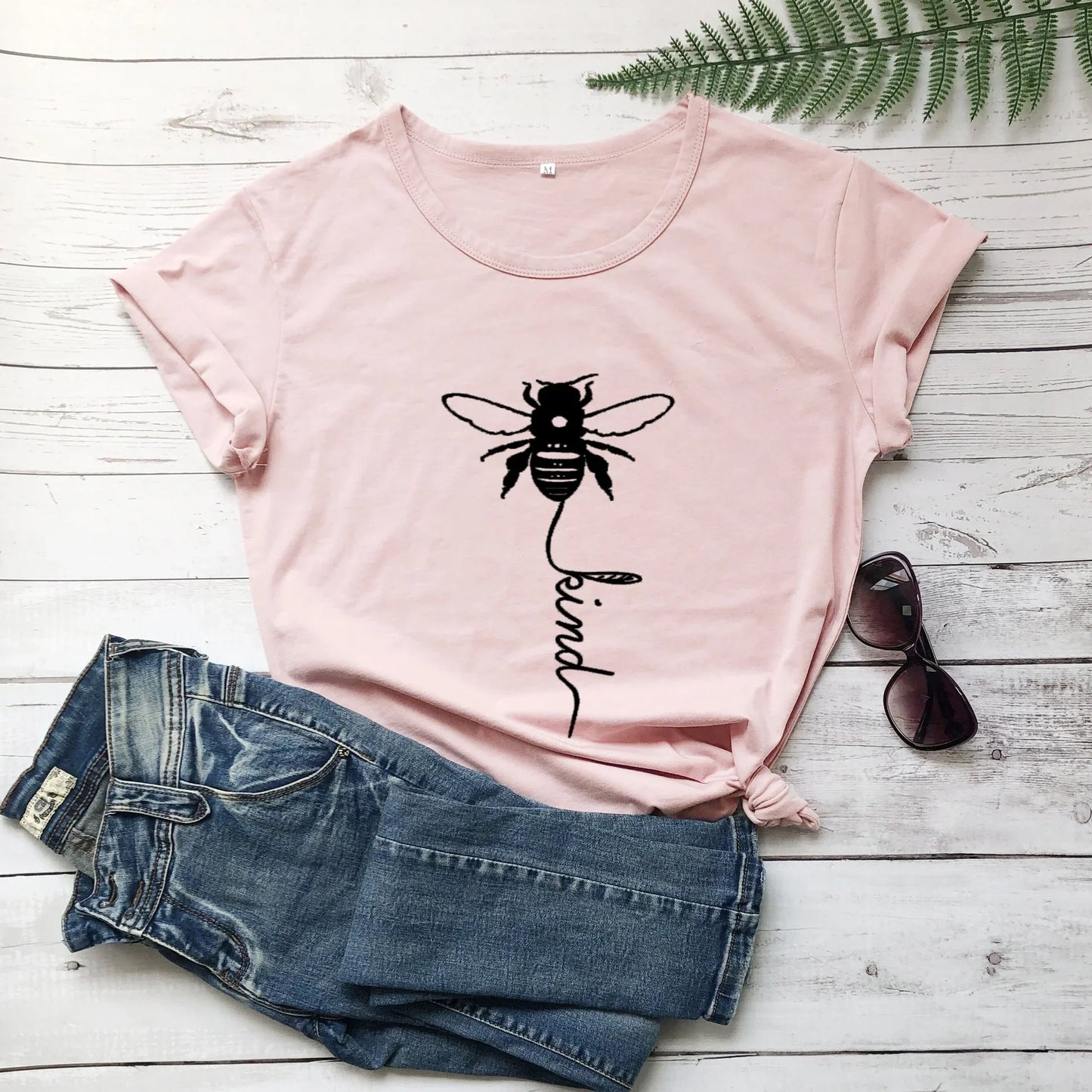 Pink graphic t-shirt with bee and 'be kind' print, paired with denim shorts and sunglasses