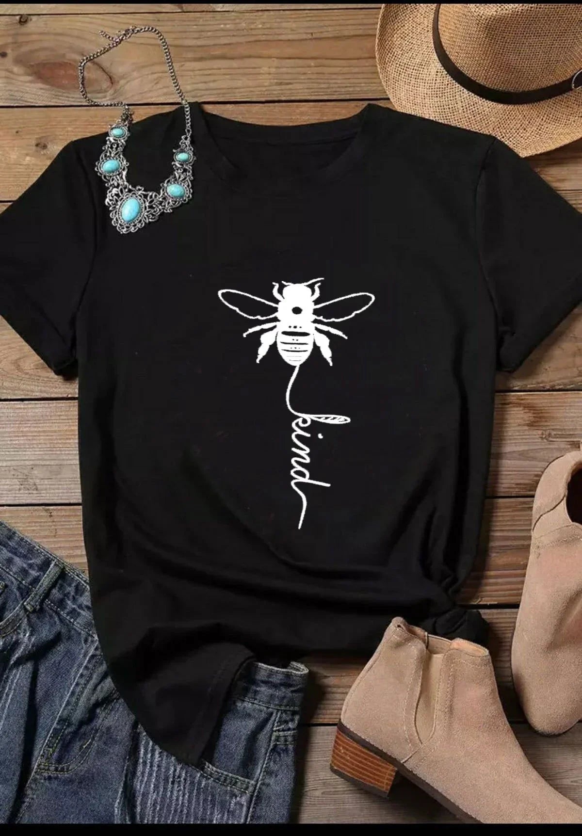 Black t-shirt with white bee and 'be kind' print, styled with boots, hat, and necklace.