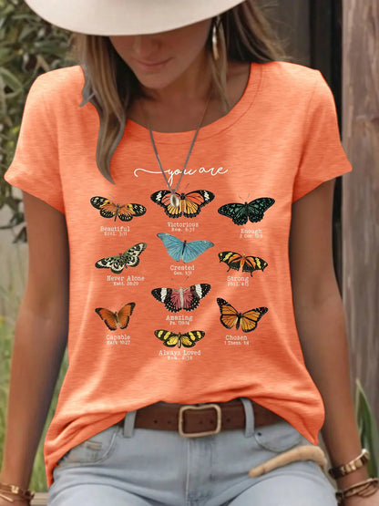 Woman wearing orange t-shirt with colorful butterfly designs and inspirational text outdoors.